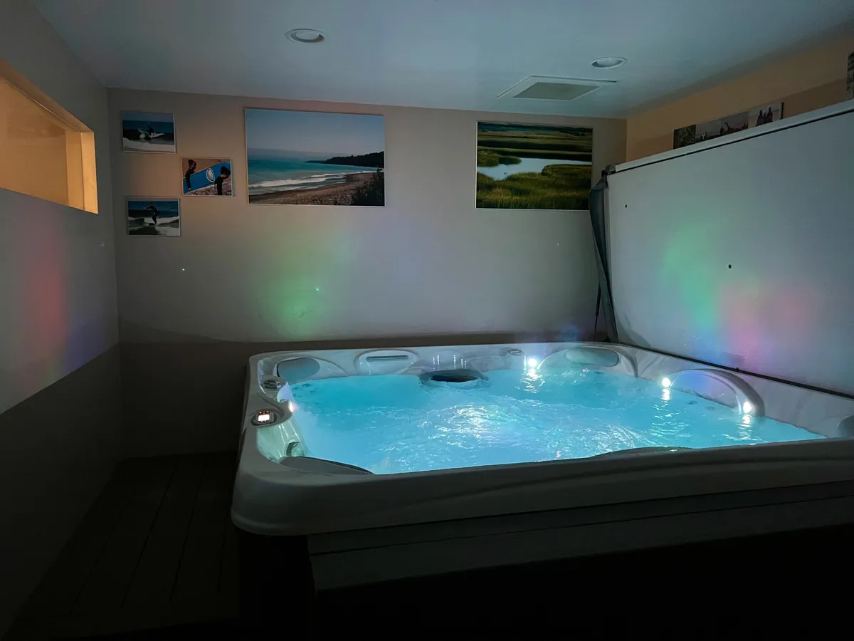 A tranquil indoor hot tub room featuring a bubbling, inviting hot tub surrounded by soft ambient lighting and tasteful wall art. The setting is serene, promising a peaceful retreat for soaking and unwinding after a day on the slopes. The decor and lighting combine to create a cozy, spa-like atmosphere suited for relaxation and connection with loved ones.
