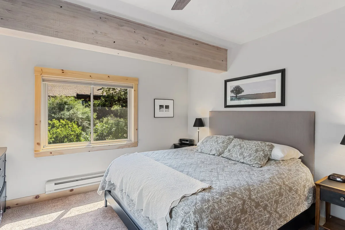 A tranquil bedroom featuring a neatly made bed, large window allowing natural light to fill the space, tasteful artwork, and matching nightstands. The serene atmosphere suggests comfort and privacy—perfect for a restful night's sleep.