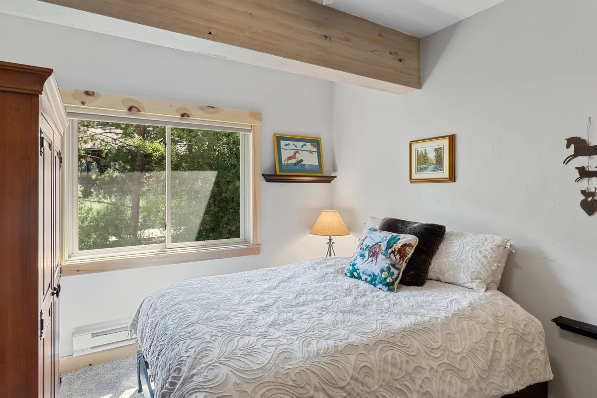 An inviting bedroom featuring a plush bed, window with a view of trees, soft lighting from a lamp, and tasteful artwork. The scene exudes warmth and tranquility, ideal for quiet mornings with coffee or unwinding after a day out.