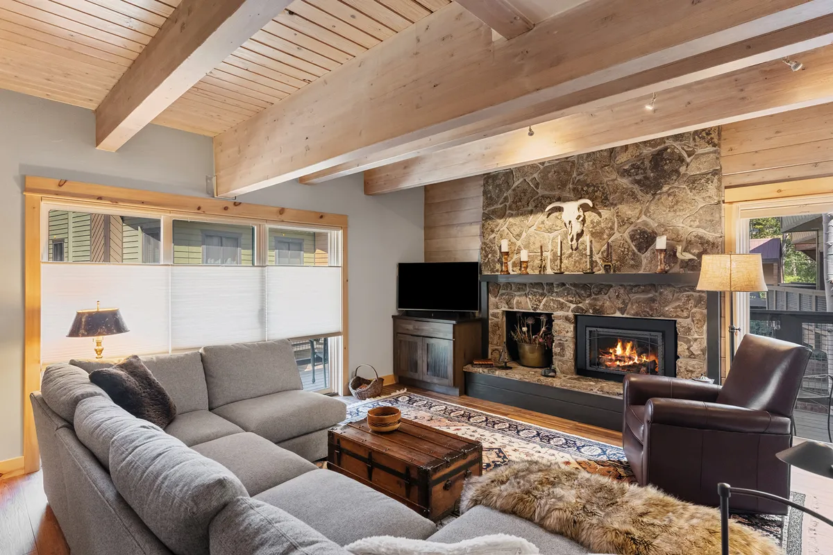 A cozy living room scene featuring a stylish gas fireplace, plush sofa, a textured area rug, and decorative accents. Sunlight streams through the windows, and the warm ambiance invites relaxation and socializing, making it an ideal spot for gathering after a day outdoors.