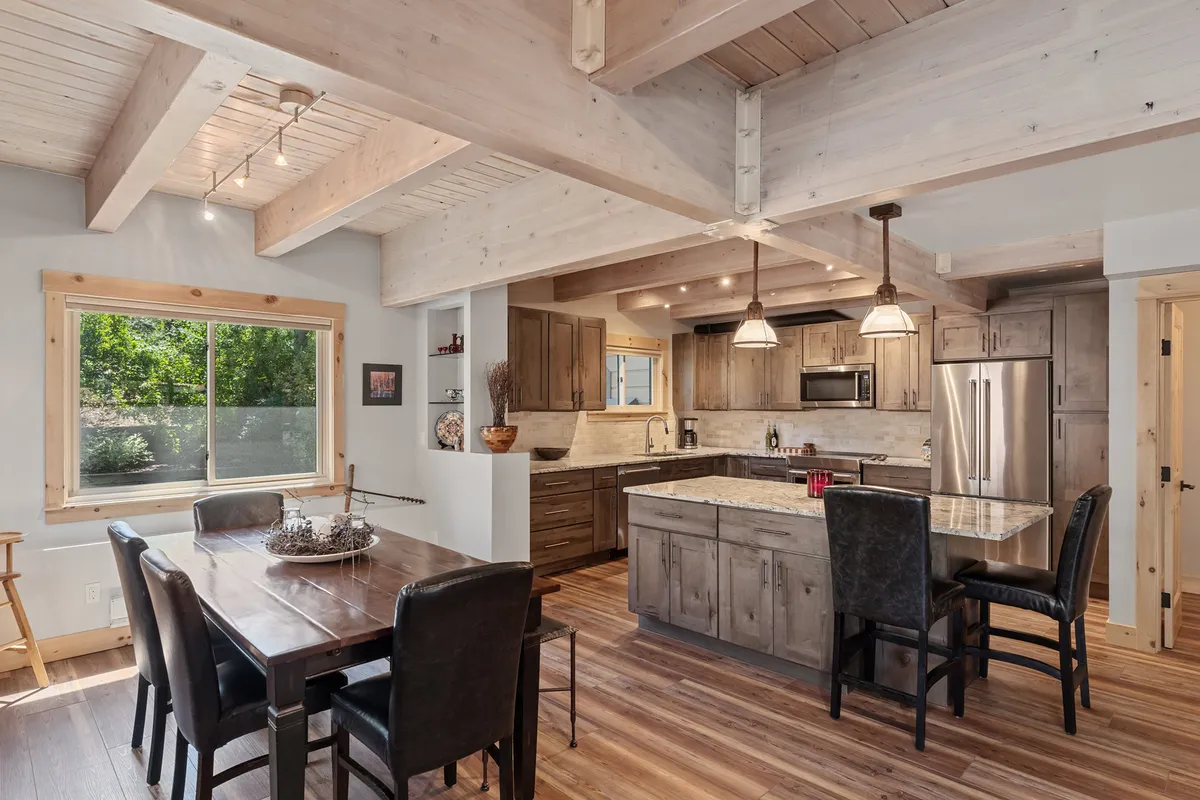 A warm, inviting dining area adjacent to a gourmet kitchen. The scene includes a spacious dining table set for a festive meal, a kitchen island ready for cooking together, and a large window letting in natural light—ideal for family meals or entertaining friends.