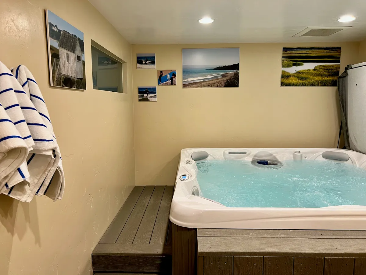 Another view of the indoor hot tub room, this time emphasizing the hot tub's proximity to plush towels and stylish wall art. The tranquil mood and inviting water highlight the space's soothing qualities and potential for social moments or quiet solitude.