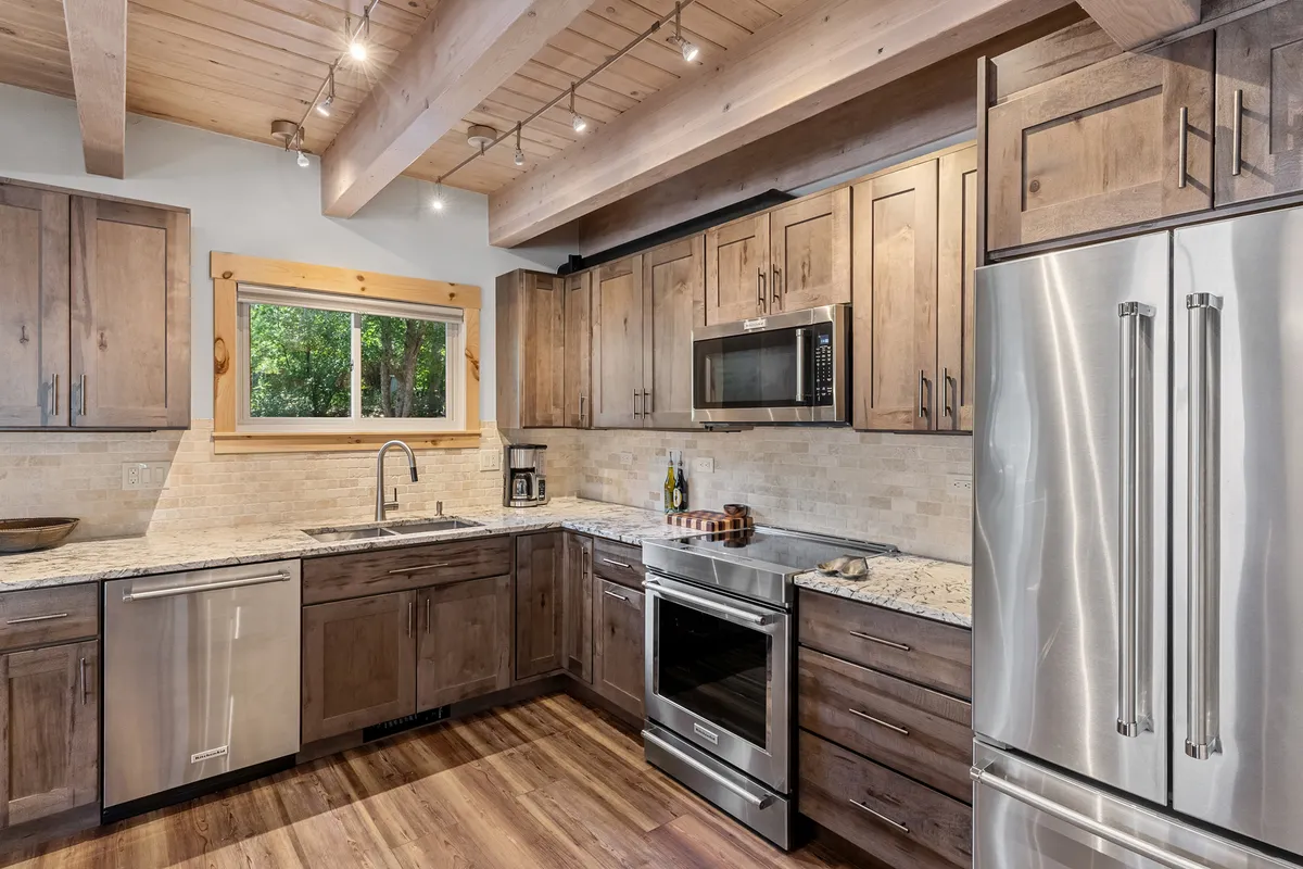 A modern kitchen with granite countertops, stainless steel appliances, wooden cabinetry, and a window providing an outdoor view. The space is designed for cooking, entertaining, and gathering, with a warm and welcoming atmosphere.